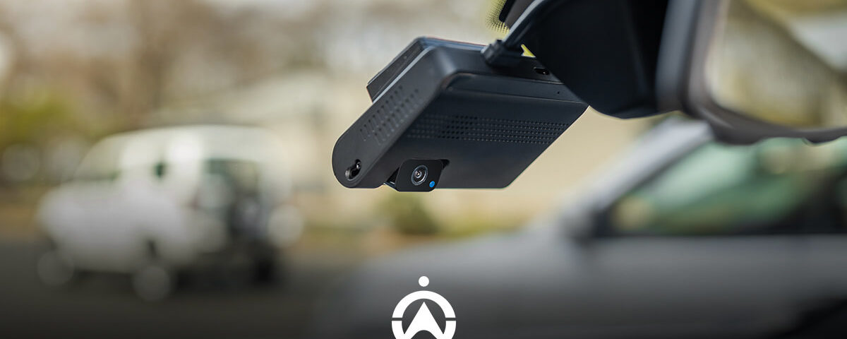 Close-up of a car's dashboard camera mounted on the windshield, with a blurred vehicle in the background.