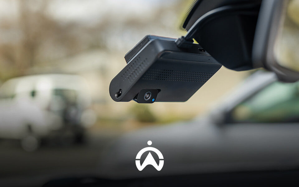 Close-up of a car's dashboard camera mounted on the windshield, with a blurred vehicle in the background.