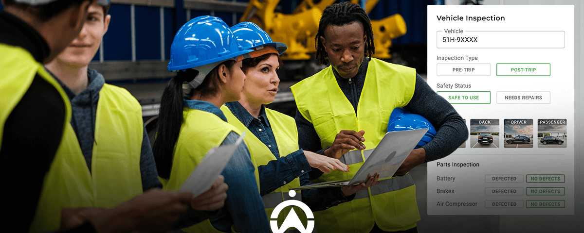 A group of workers in yellow vests and hard hats conducting a vehicle inspection with a laptop and digital checklist in a warehouse.