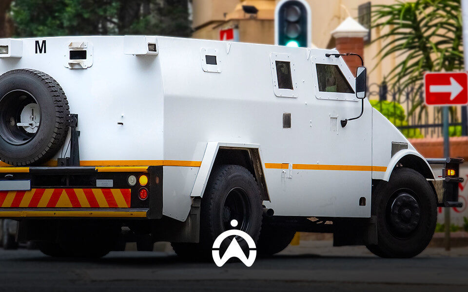 A white armored vehicle with a spare tire on the back, parked near a traffic light and directional sign in an urban setting.