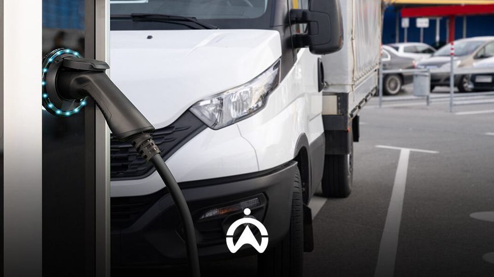 An electric truck is connected to a charging station, showcasing the vehicle's charging plug and illuminated indicators in a parking lot.