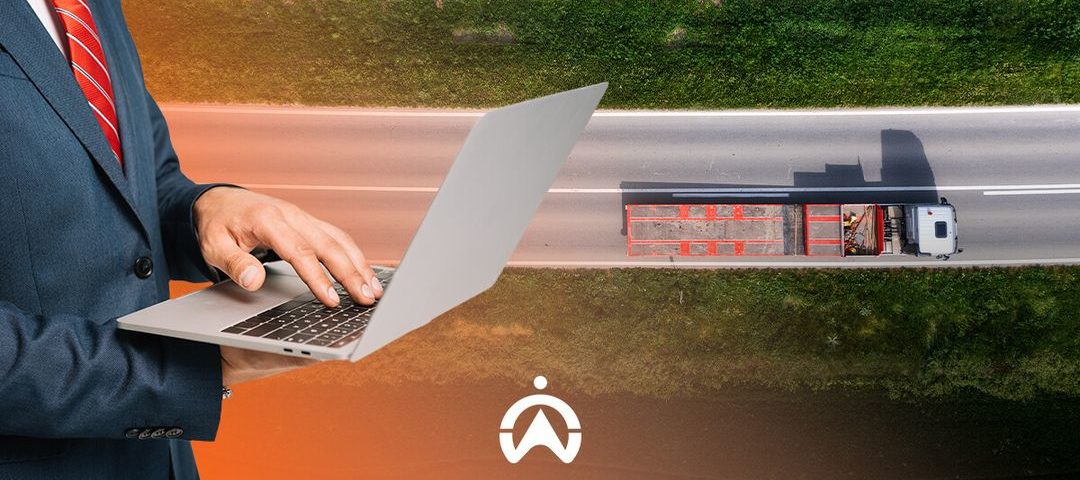A businessman in a suit uses a laptop over an aerial image of a truck driving on a road, symbolizing logistics and technology integration.
