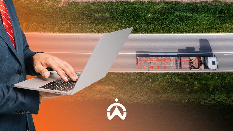 A businessman in a suit uses a laptop over an aerial image of a truck driving on a road, symbolizing logistics and technology integration.