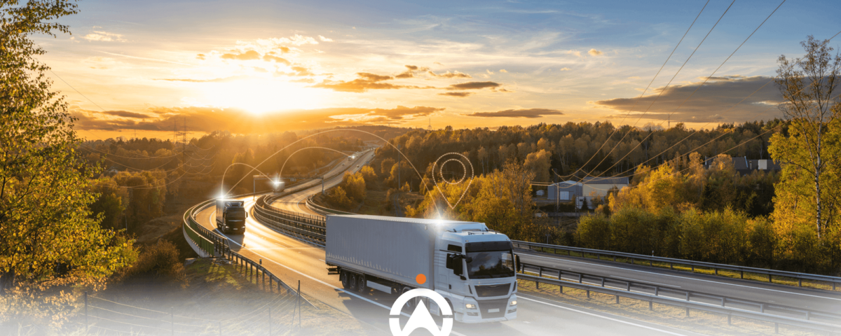 Trucks driving on a winding highway at sunset, surrounded by colorful autumn foliage and power lines in the background.