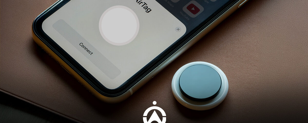 A smartphone displaying an "AirTag" connection screen next to an actual AirTag device on a brown leather surface.