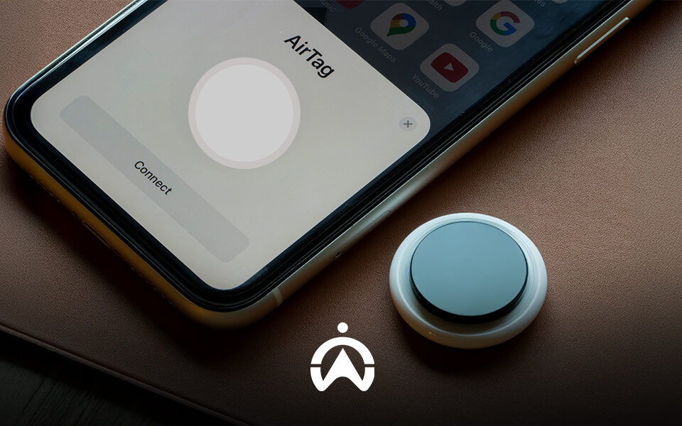 A smartphone displaying an "AirTag" connection screen next to an actual AirTag device on a brown leather surface.